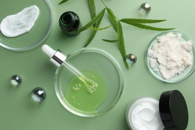 Petri dishes with cosmetic products, pipette and leaves on green background, flat lay