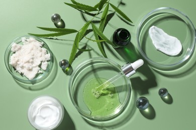 Petri dishes with cosmetic products, pipette and leaves on green background, flat lay