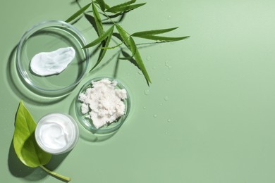 Petri dishes with cosmetic products and leaves on green background, flat lay. Space for text