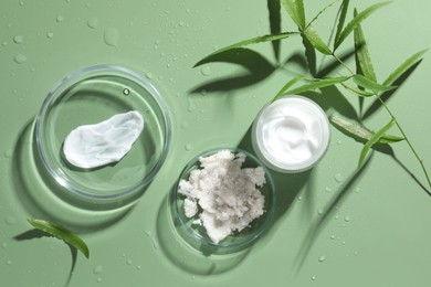 Petri dishes with cosmetic products and leaves on green background, flat lay