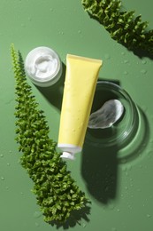 Photo of Petri dish with cosmetic products and fern leaves on green background, flat lay