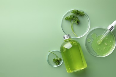 Petri dishes with cosmetic product, bottle, pipette and parsley on green background, flat lay. Space for text