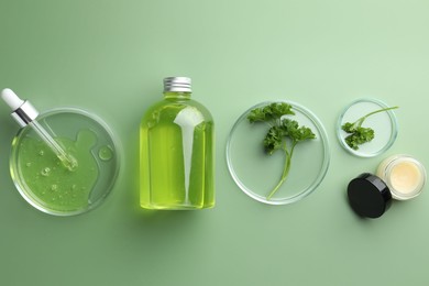 Photo of Petri dishes with cosmetic products, pipette and parsley on green background, flat lay