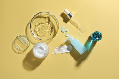 Photo of Petri dishes with cosmetic products and pipette on yellow background, flat lay