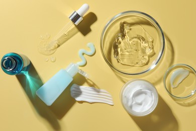 Photo of Petri dishes with cosmetic products and pipette on yellow background, flat lay