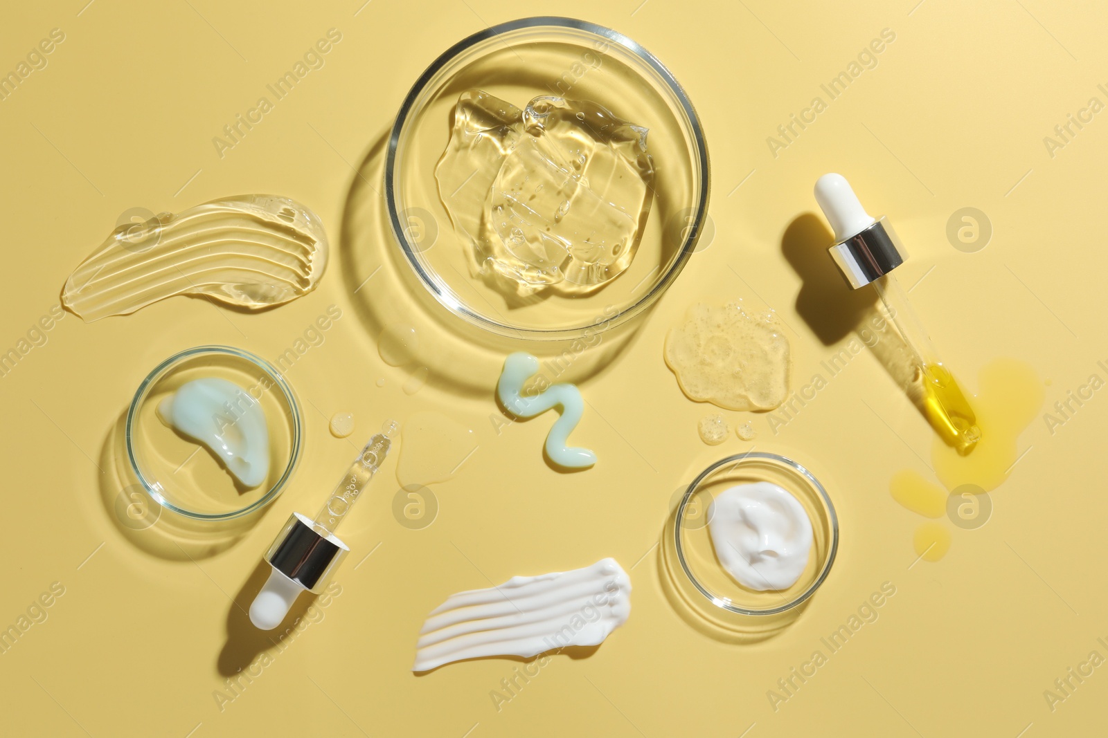 Photo of Petri dishes with cosmetic products and pipettes on yellow background, flat lay