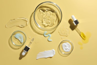 Petri dishes with cosmetic products and pipettes on yellow background, flat lay