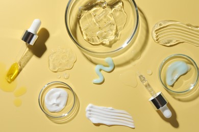 Photo of Petri dishes with cosmetic products and pipettes on yellow background, flat lay