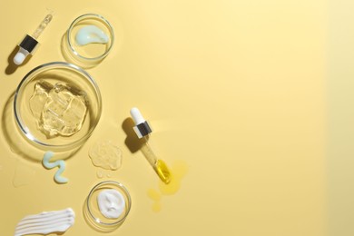 Photo of Petri dishes with cosmetic products and pipettes on yellow background, flat lay. Space for text