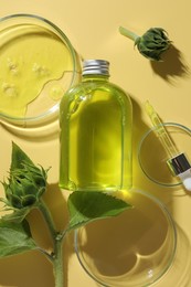 Photo of Petri dishes with cosmetic product, bottle, pipette and sunflowers on yellow background, flat lay