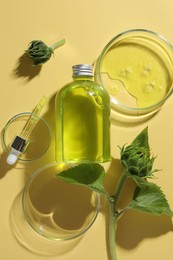 Petri dishes with cosmetic product, bottle, pipette and sunflowers on yellow background, flat lay