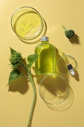 Petri dishes with cosmetic product, bottle, pipette and sunflowers on yellow background, flat lay