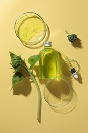 Petri dishes with cosmetic product, bottle, pipette and sunflowers on yellow background, flat lay