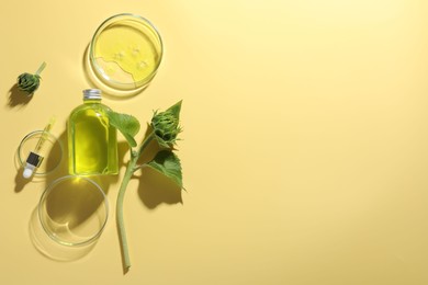 Petri dishes with cosmetic product, bottle, pipette and sunflowers on yellow background, flat lay. Space for text