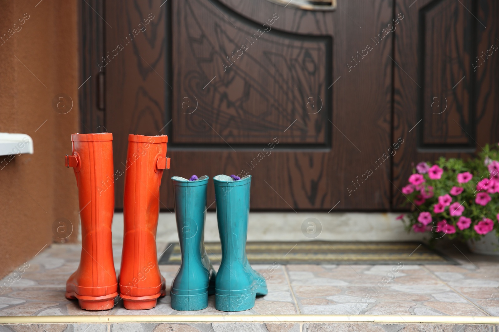 Photo of Two pairs of rubber boots on doorstep near entrance outdoors