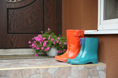 Photo of Two pairs of rubber boots on doorstep near entrance outdoors