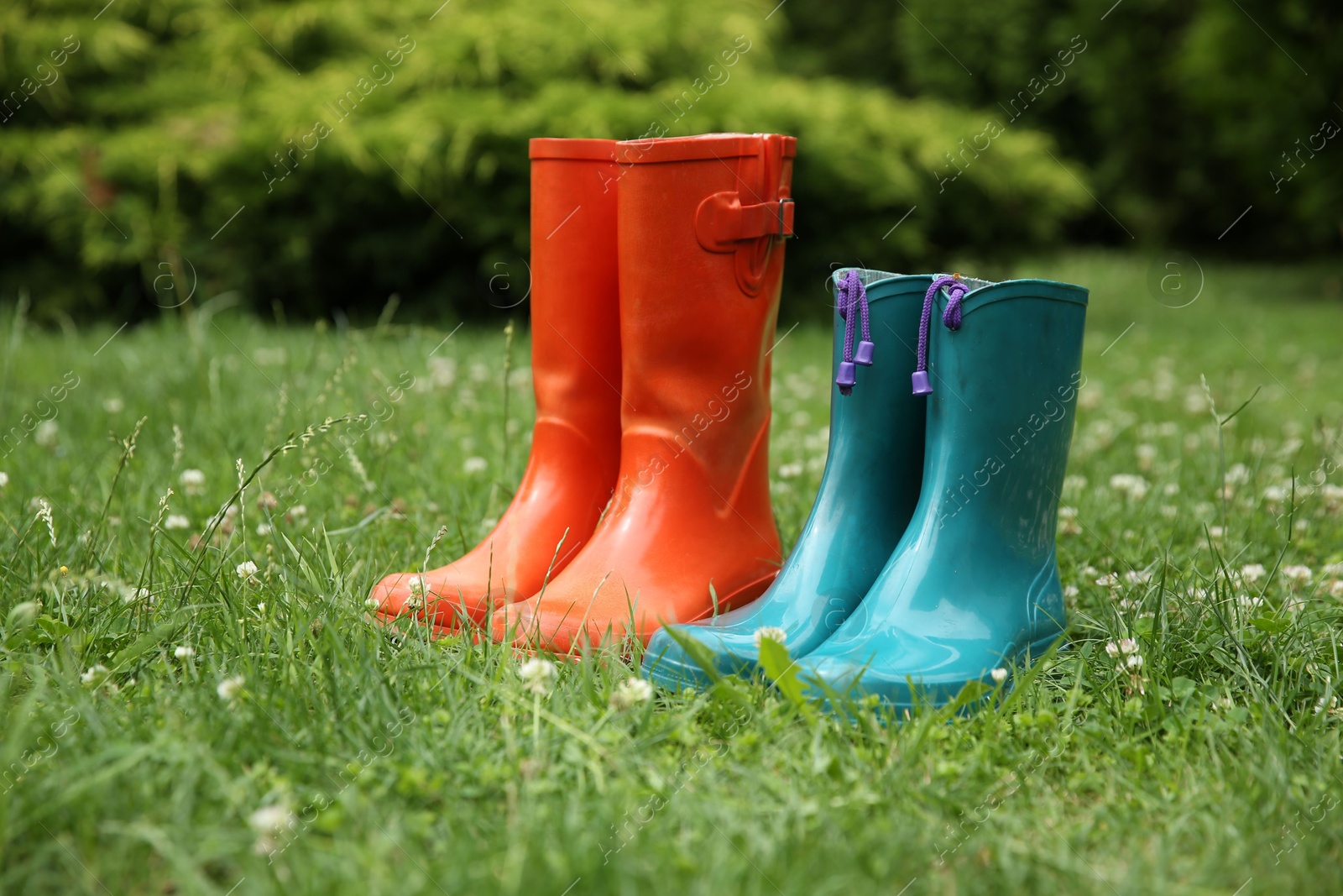 Photo of Two pairs of rubber boots on green grass outdoors