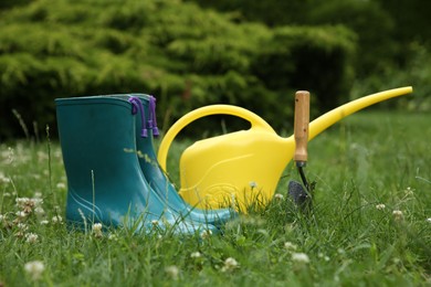 Photo of Rubber boots and gardening tools on green grass outdoors