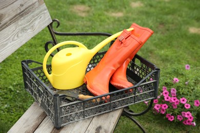 Photo of Orange rubber boots and gardening tools in crate outdoors