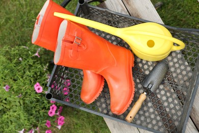 Orange rubber boots and gardening tools in crate outdoors, top view