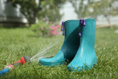 Photo of Bright rubber boots under water pressure on green grass outdoors