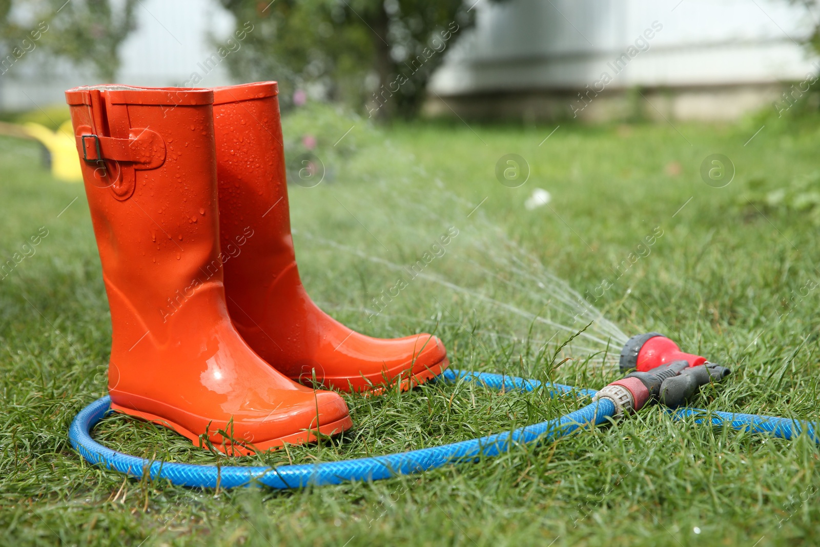 Photo of Orange rubber boots under water pressure on green grass outdoors