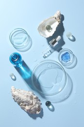 Petri dishes with cosmetic product, pipette and seashells on light blue background, flat lay