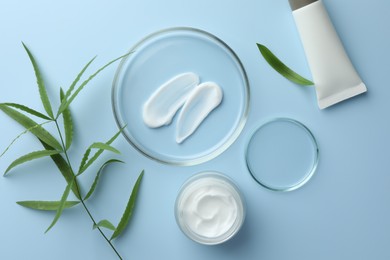 Photo of Petri dishes with cosmetic product and leaves on light blue background, flat lay