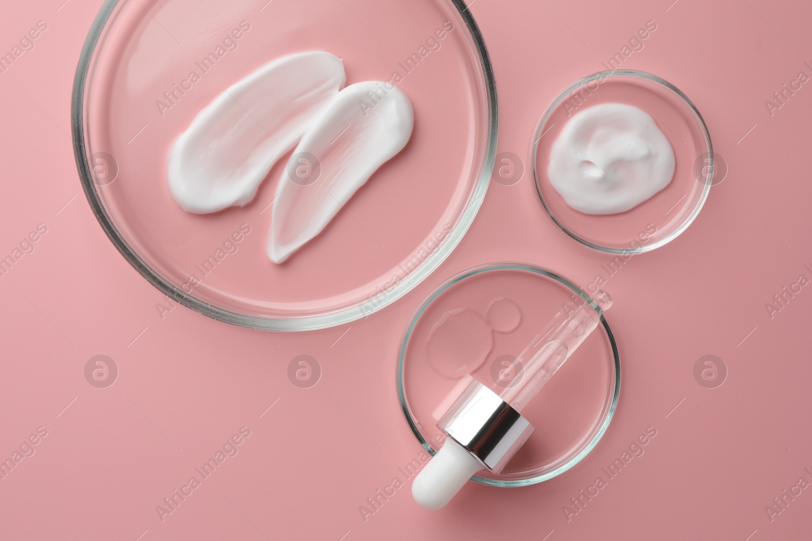 Photo of Petri dishes with cosmetic products and pipette on pink background, flat lay