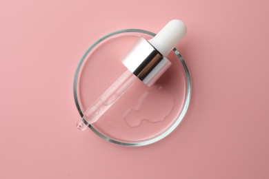 Photo of Petri dish with cosmetic product and pipette on pink background, top view