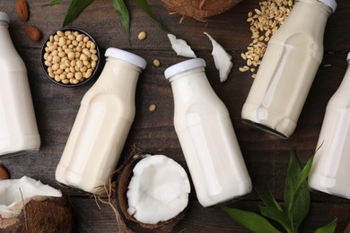 Photo of Different types of vegan milk in bottles with ingredients and green leaves on wooden table, flat lay