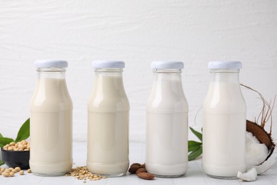 Different types of vegan milk in bottles and ingredients on white tiled table