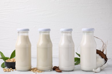 Photo of Different types of vegan milk in bottles and ingredients on white tiled table