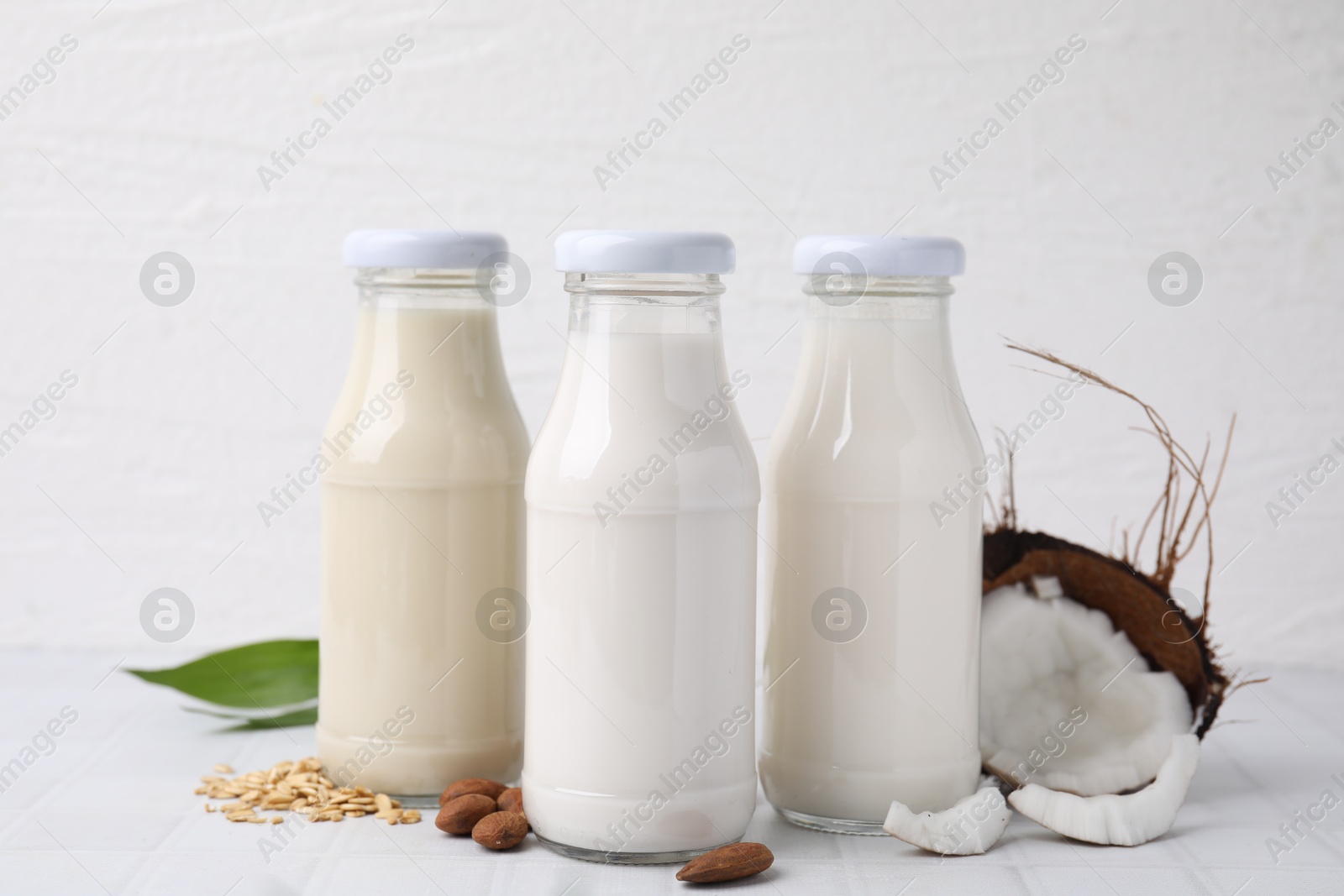 Photo of Different types of vegan milk in bottles and ingredients on white tiled table