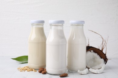 Different types of vegan milk in bottles and ingredients on white tiled table