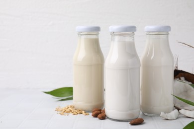 Photo of Different types of vegan milk in bottles and ingredients on white tiled table, space for text