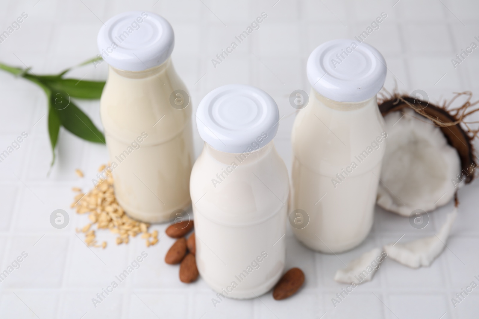 Photo of Different types of vegan milk in bottles and ingredients on white tiled table, closeup