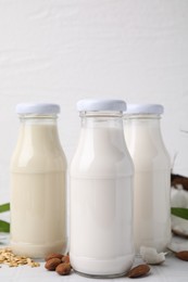 Photo of Different types of vegan milk in bottles and ingredients on white tiled table, closeup