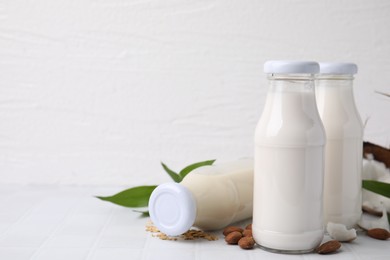 Photo of Different types of vegan milk in bottles with ingredients on white tiled table, space for text