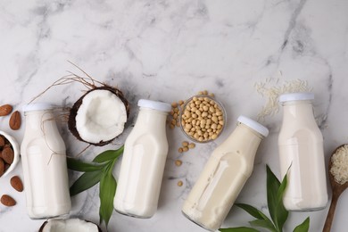 Photo of Different types of vegan milk in bottles with ingredients and leaves on white marble table, flat lay