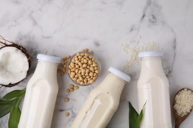 Photo of Different types of vegan milk in bottles with ingredients and leaves on white marble table, flat lay