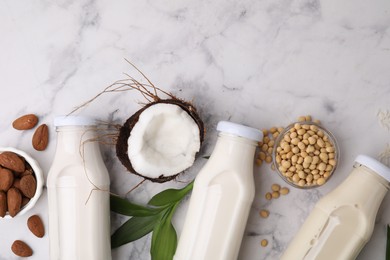 Photo of Different types of vegan milk in bottles with ingredients and leaves on white marble table, flat lay