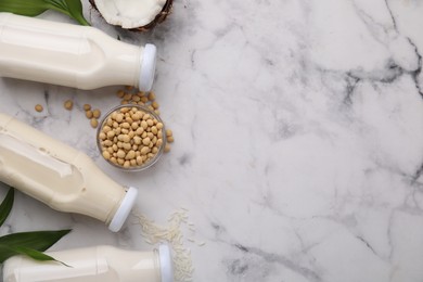 Photo of Different types of vegan milk in bottles with ingredients and green leaves on white marble table, flat lay. Space for text