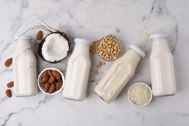 Different types of vegan milk in bottles and ingredients on white marble table, flat lay