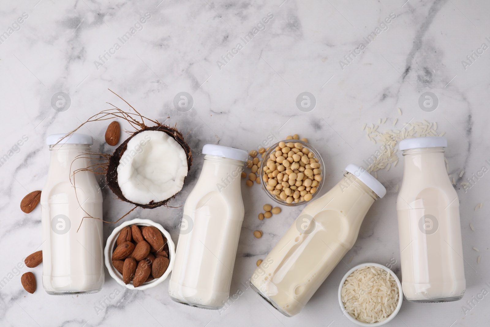 Photo of Different types of vegan milk in bottles and ingredients on white marble table, flat lay