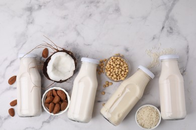 Different types of vegan milk in bottles and ingredients on white marble table, flat lay