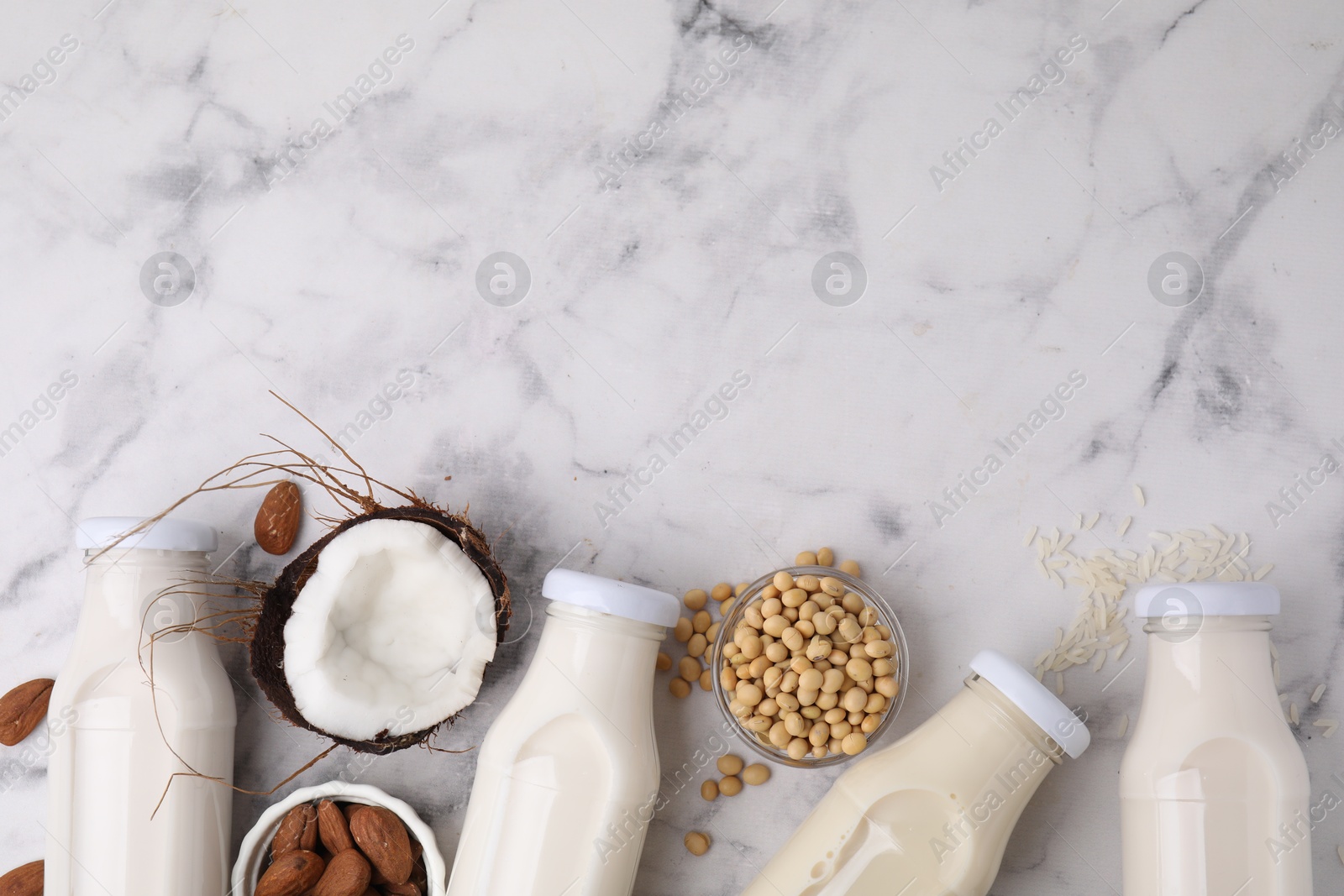 Photo of Different types of vegan milk in bottles and ingredients on white marble table, flat lay. Space for text