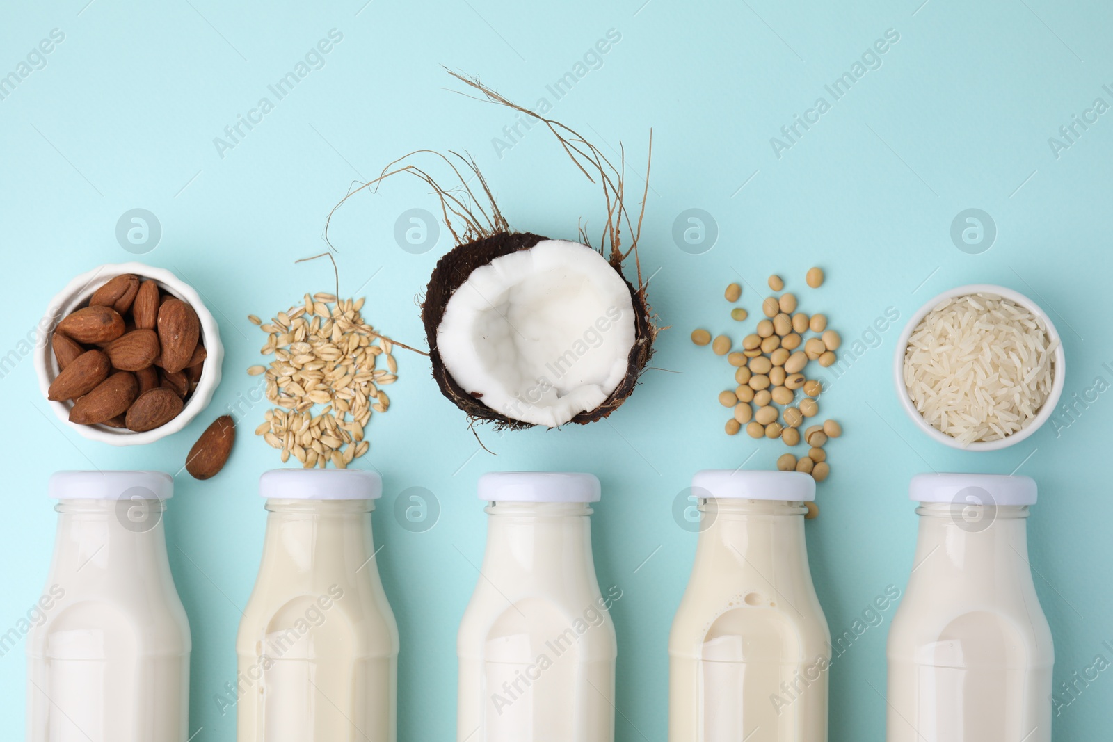 Photo of Different types of vegan milk in bottles and ingredients on light blue table, flat lay