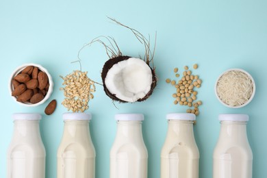 Different types of vegan milk in bottles and ingredients on light blue table, flat lay