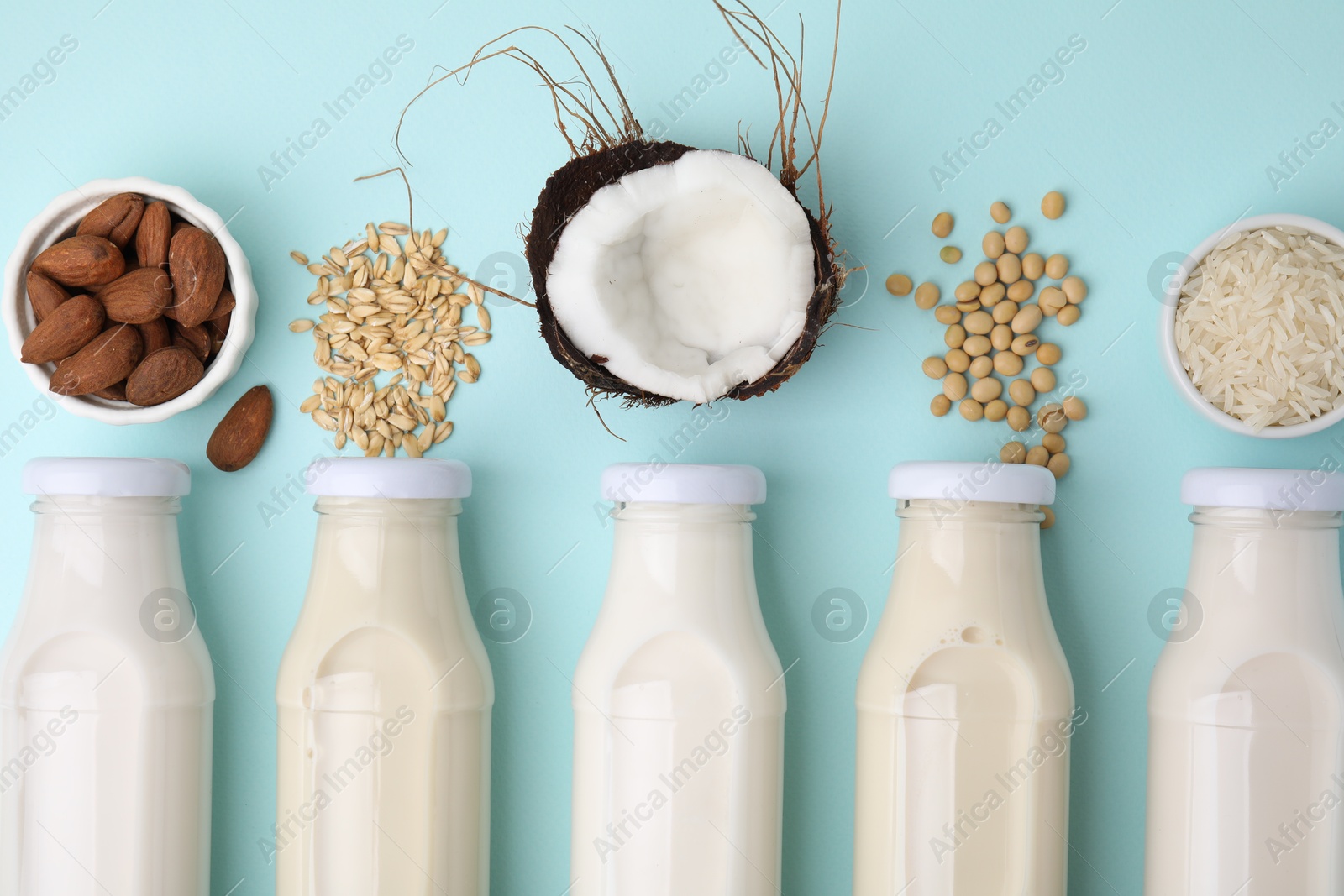 Photo of Different types of vegan milk in bottles and ingredients on light blue table, flat lay